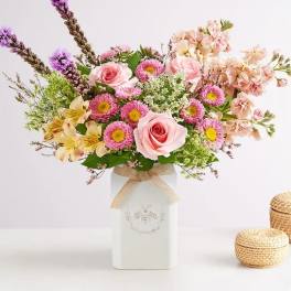 Pink and peach flower arrangement in a white vase with a ribbon