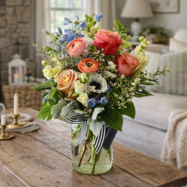 Mixed bouquet of roses, ranunculus, and blue flowers in a glass vase