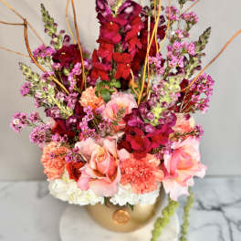 Tall floral arrangement with pink roses and magenta snapdragons in a gold vase