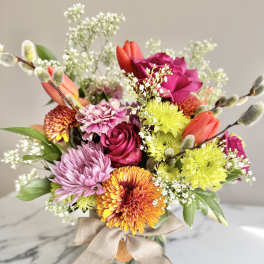 Bright mixed bouquet of roses, tulips, mums, and carnations in a glass vase with a bow