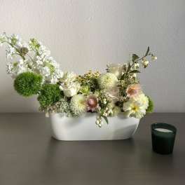 White floral arrangement in a low rectangular vase with green pom-pom accents