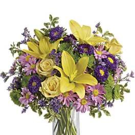 Yellow lilies and purple daisies in a clear glass vase