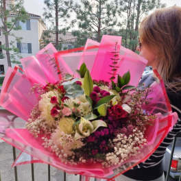 Large bouquet of mixed pink, white, and red flowers wrapped in bright pink paper
