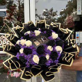 Bouquet of black and cream roses with purple filler and black-gold wrapping