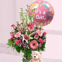 Pink flower arrangement in a glass vase with It's a Girl balloon and teddy bear