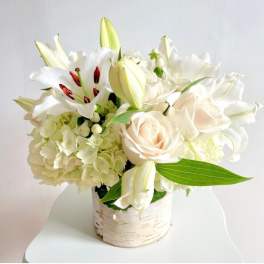 White floral arrangement with roses, lilies, and hydrangeas in a birch-style container
