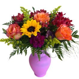 Mixed bouquet with sunflowers, roses, and red blooms in a purple vase
