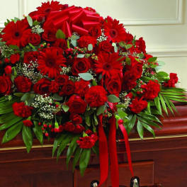 Red casket spray of roses and gerbera daisies with large greenery and a red bow
