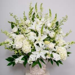 Large all-white arrangement of lilies, roses, hydrangeas, and snapdragons in a white woven basket.