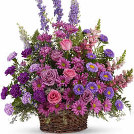 Tall basket arrangement of purple and pink roses, daisies, carnations, asters, and snapdragons