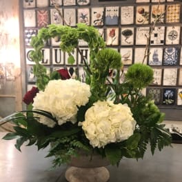 White hydrangeas and red roses in a low pedestal bowl with greenery