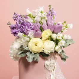 Lavender, white, and pale yellow flowers in a pink hatbox with lace ribbon
