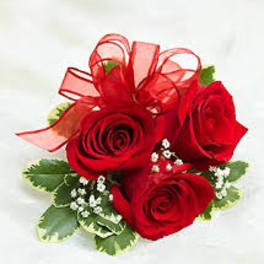 Small cluster of red roses with white filler flowers and a red ribbon bow.