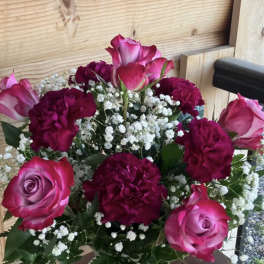 Arrangement of pink roses, deep red carnations, and white filler flowers in a frosted glass vase.