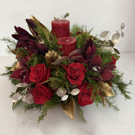 Red roses and burgundy orchids arranged with candles and greenery