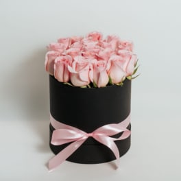 Pink roses arranged in a black round box with a pink ribbon