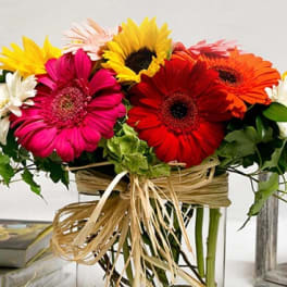 Bright gerbera daisies arranged in a clear square vase with raffia ribbon