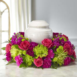 Pink roses and magenta flowers arranged around a white urn