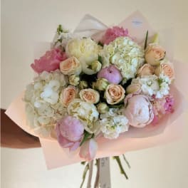 Hand-tied bouquet of pink and white flowers wrapped in pale pink paper