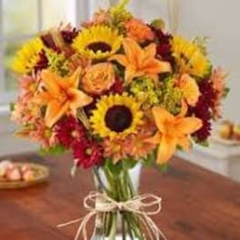 Bouquet of sunflowers, orange lilies, and mixed fall flowers in a glass vase
