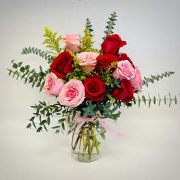 Red and pink rose arrangement with eucalyptus in a clear glass vase tied with a pink ribbon