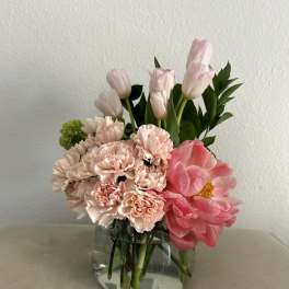 Pink tulips and carnations arranged in a clear glass vase