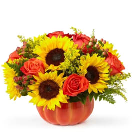 Sunflowers and red roses arranged in an orange pumpkin vase