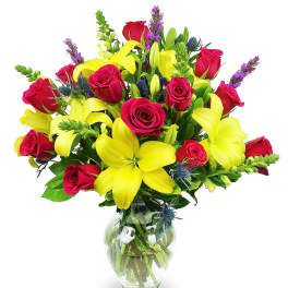 Bouquet of yellow lilies and red roses with purple accents in a clear glass vase