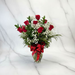 Red roses in a glass vase with baby's breath and a red ribbon