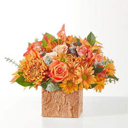 Orange and pink flower arrangement in a leaf-patterned square vase