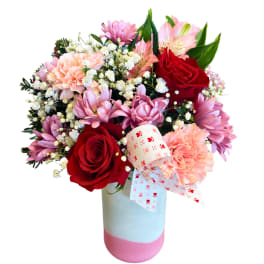 Bouquet of red roses, pink carnations, and purple daisies in a pastel vase