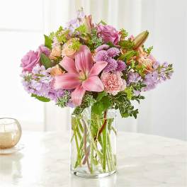Pink lilies and mixed pastel flowers in a clear glass vase