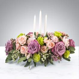 Low floral centerpiece with pink and purple roses and three white candles