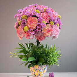 Pink and peach flowers in a patterned vase with green foliage