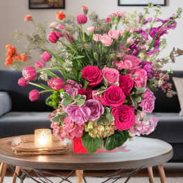 Pink and purple mixed flower arrangement in a red box on a table