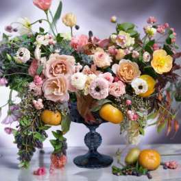 Mixed pastel floral arrangement in a dark blue pedestal vase with fruit accents