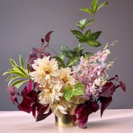 Arrangement of cream dahlias and pink orchids in a gold vase