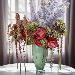 Tall floral arrangement in a green vase with red anthuriums and lavender blooms
