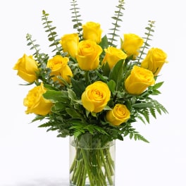 Arrangement of bright yellow roses with greenery in a clear glass vase
