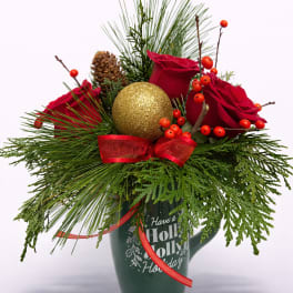 Holiday mug arrangement with red roses, pine branches, berries, and a gold ornament ball