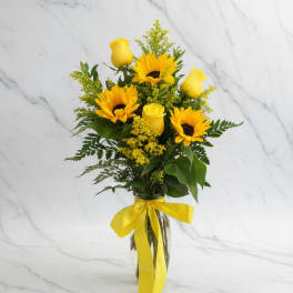 Tall arrangement of yellow sunflowers and roses in a clear vase with a yellow ribbon bow