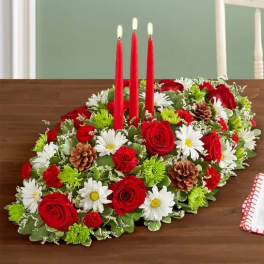 Oval floral centerpiece with red candles, red roses, white daisies, and pinecones