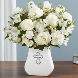 White roses and mixed white flowers arranged in a white vase with a cross emblem