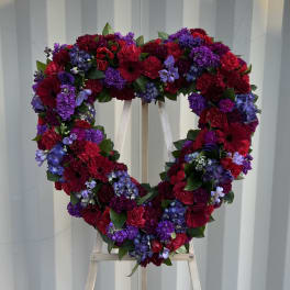 Heart-shaped floral wreath with red, purple, and blue flowers on a stand