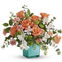Peach roses and white flowers in a turquoise glass vase