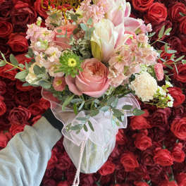 Pink and white bouquet with a birthday topper against a wall of red roses