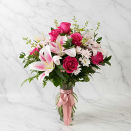 Pink roses and lilies in a glass vase with a pink ribbon
