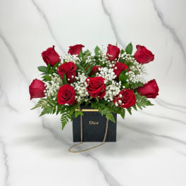 Red roses arranged in a black Dior gift box with a gold chain
