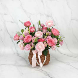 Pink rose and ranunculus arrangement in a wicker basket with a ribbon