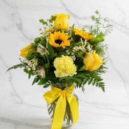 Yellow roses and mixed flowers in a glass vase with a yellow ribbon